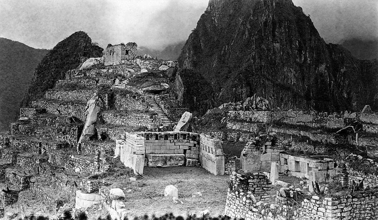 A general view of the Sacred Plaza, the site of the finest structures at Machu Picchu. In the center is the Chief Temple, and at the right the Temple of the Three Windows. Above them is the Sacred Hil